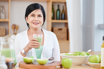 Portrait of mature Asian woman with glass of fresh smoothie