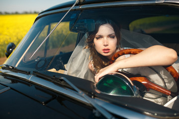 Fototapeta na wymiar Stunning bride looks through the car's window leaning on a wheel
