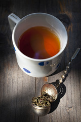 Cup of tea with tea leafs  in a metal strainer on a wooden table. Old fashioned, Vertical, sunlit