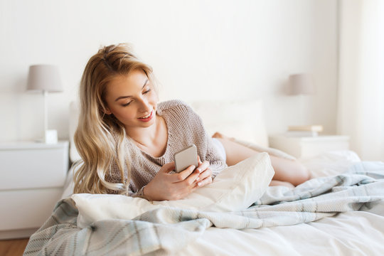 happy young woman with smartphone in bed at home
