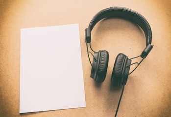 Headphone with brown and white paper note on wood desk in music studio.