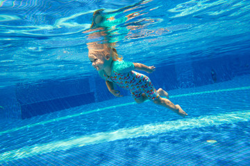 Little girl swimming underwater in the pool and smiling