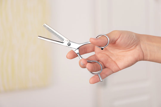 Hairdresser holding professional scissors on blurred background