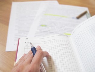 Hand holding a pen over textbook on wooden background. Studying and homework concept.