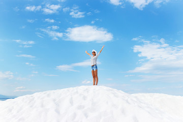 Young woman standing on white beach with her arms outstretched over horizon. She is looking towards the sun.