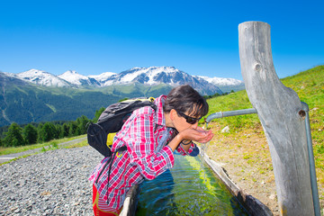 Girl hiker quenches thirst at the fountain during a mountain tre