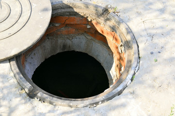 Concrete cesspit with an open hatch on the ground in the summer