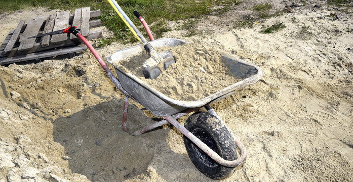 A pile of sand, a shovel and a construction truck for transporta