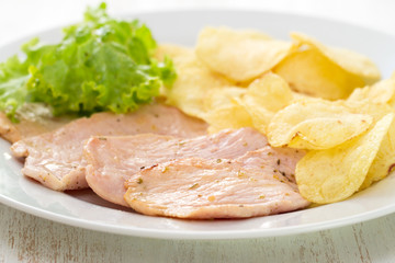 fried meat with potato chips and fresh salad on white dish on white wooden background