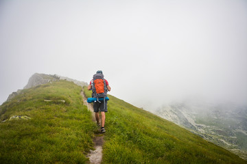 Young Man Traveler with backpack, walking in cloudy weather.