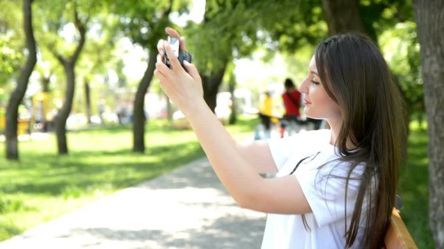 smiling young woman making selfie photo in park with old film camera