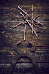 Old rusty tongs with nails on wooden boards background