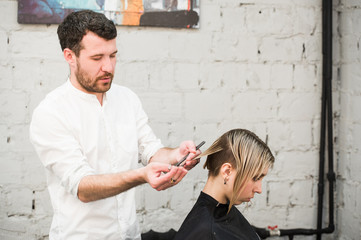 hairdresser cuts hair with scissors on crown of handsome satisfied client in professional hairdressing salon