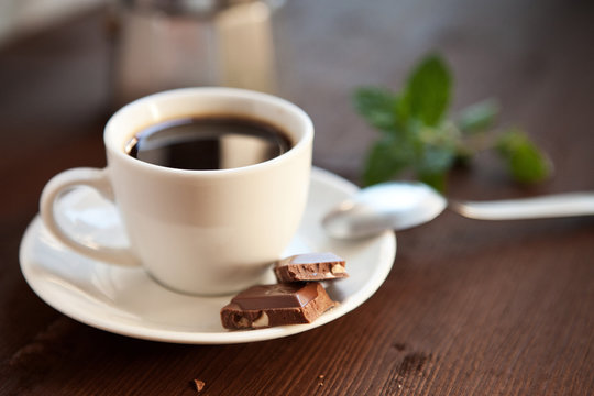 Filiżanka czarnej kawy z kostkami czekolady i listkiem mięty