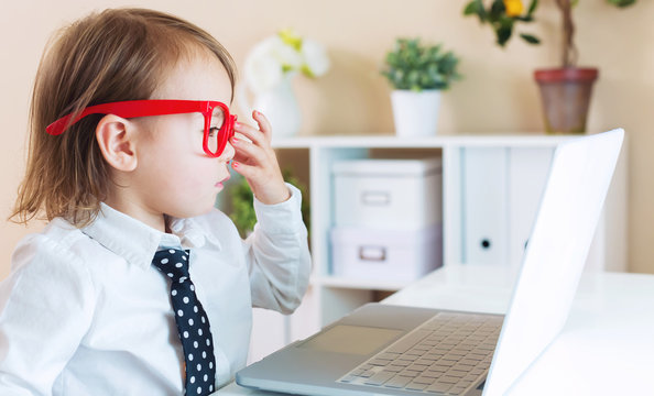 Toddler girl wearing big red glasses while using her laptop