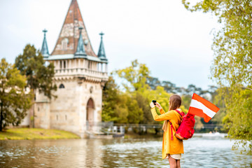 Young female traveler with austrian flag taking picture in front of Franzensburg castle in Laxenburg town. Traveling in Austria