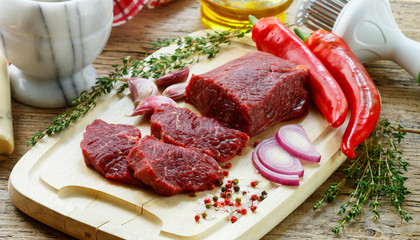 Beef. Fresh raw meat on a cutting Board, olive oil, garlic, hot pepper, thyme and spices on the table
