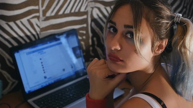 Sadness teenage girl at laptop looks at camera