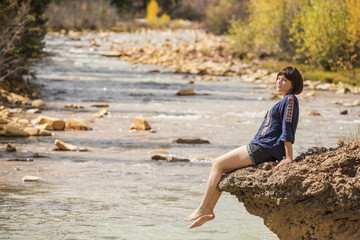 White water Mineral Creek stream in Colorado, USA during the fall with golden aspens and woman on edge dipping feet in water