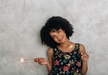 African American young woman with sparklers at gray background