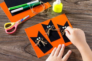 The child create a greeting card Halloween black cat out of pape