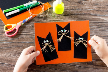The child create a greeting card Halloween black cat out of pape