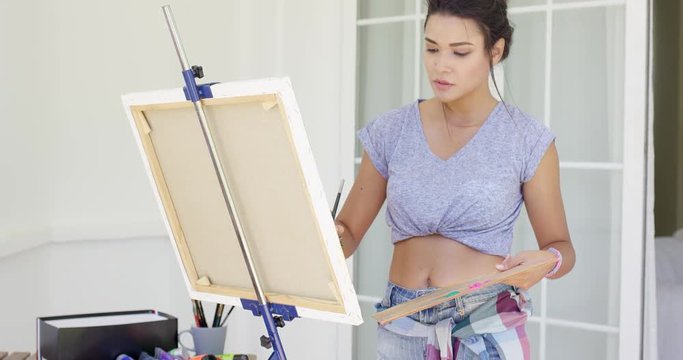 Serious young female artist painting outdoors on a patio working on a canvas on an easel