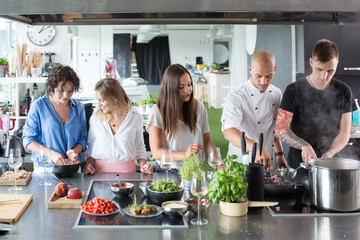 Men cooking and women talking and smiling in modern kitchen