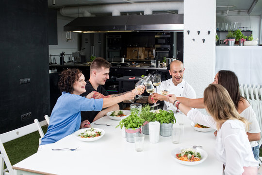 Cheerful people having dinner and toasting with glasses