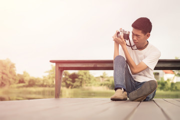 Young photographer sitting on the wooden deck beside the water with sunrise.