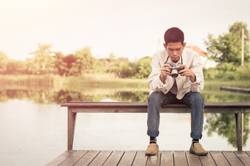Young photographer sitting on the wooden deck beside the water with sunrise. - Powered by Adobe
