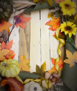 Cheerful fall or autumn border with fall leaves, nuts, sunflowers and squashes with green folded burlap and gold ribbon on a wooden background. Vintage filter applied. Copy space