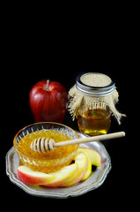 Rosh Hashanah low key image of honey and apple on a pewter plate. The honey is in a crystal bowl and in a canning jar with burlap top. All on a black background with copy space.