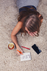 Beautiful girl lying on the carpet at home and writing in a notebook next to her cup of tea with lemon stand, top view