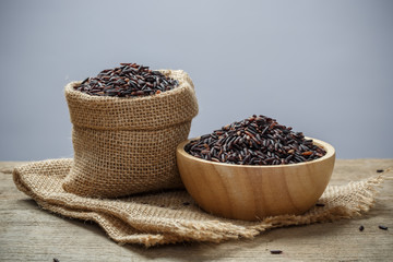 Rice berry or uncooked brown rice in bowl and burlap sack on woo
