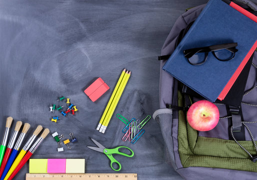 Back to school supplies and backpack on chalkboard background