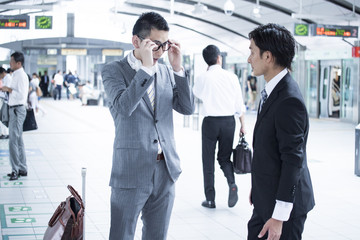 Two young businessmen have a stand talking at the station