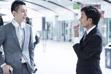 Two young businessmen have a stand talking at the station