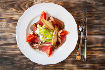 Salad with slices of smoked meat and vegetables on a white plate