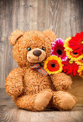 Flowers and a teddy bear on wooden background