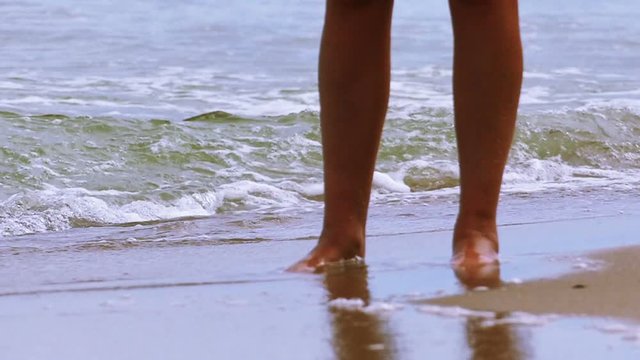 Slow motion.  Female legs stand on the sea coast among waves