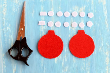 Cut pieces of felt for Christmas ball ornament, scissors on blue wooden background. Make a felt...