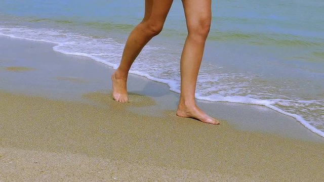 Slow motion.  Female legs  go  on  sea coast among waves