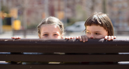 boy with blonde girl hiding on a street bench
