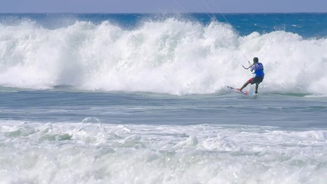 Professional kitesurfer doing tricks on high waves in ocean. Sport background