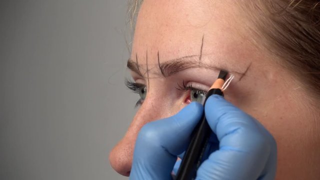 Microblading procedure. Master marks out customer's eyebrows