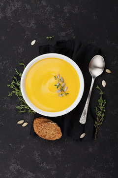 Pumpkin soup decorated seeds and thyme in white bowl on black table top view. Flat lay styling.