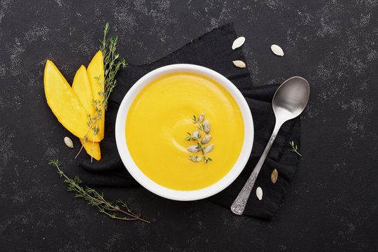Pumpkin soup decorated seeds and thyme in white bowl on vintage black table top view. Flat lay styling.