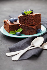 Brownie stack decorated blueberries and green mint leaves. Chocolate cake in turquoise plate on vintage black table. Homemade pastry for dessert.