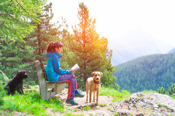 Girl reads a book on a bench in the mountains in the company of